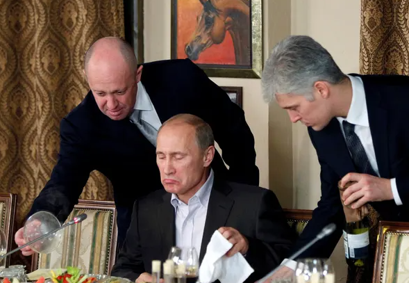 Prigozhin (majtas) ndihmon Vladimir Putin gjatë një darke me studiues dhe gazetarë të huaj jashtë Moskës në nëntor 2011. Fotografia: Reuters